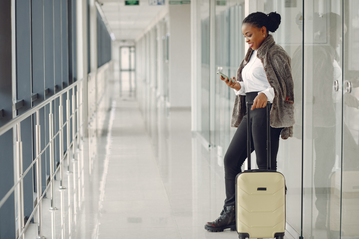 A smiling Black woman with her luggage at the airport, checking her phone while travelling